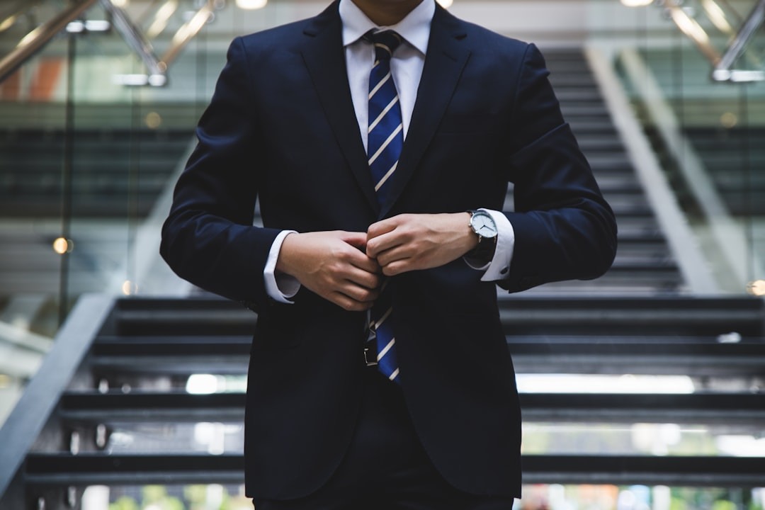 Businessperson in a suit adjusts tie while standing on a staircase indoors.